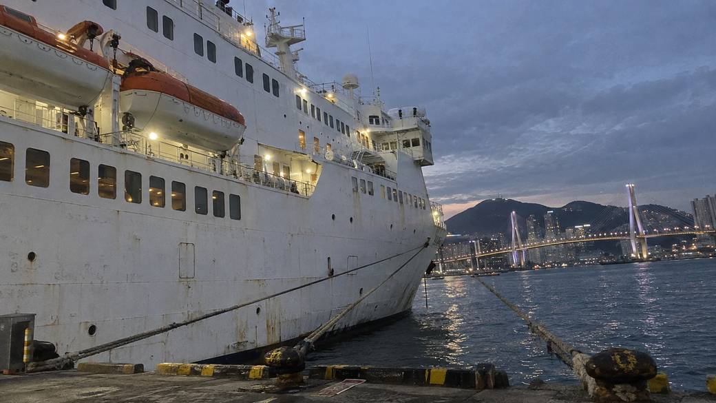 A large white overnight ferry docked at Busan Port International Passenger Terminal at dusk, the harbour bridge lit in the