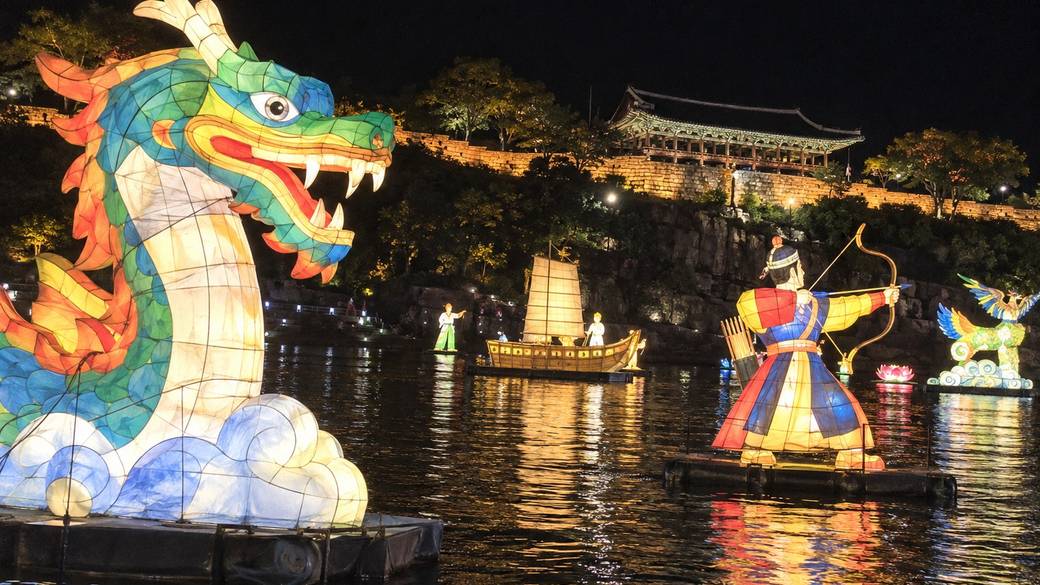 Glowing floating lanterns on the Namgang river at night with Jinju Fortress and its pavilion lit on the bank