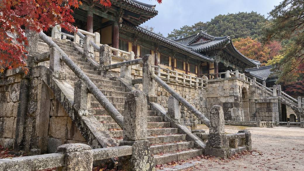 Bulguksa Temple in Gyeongju on an autumn morning, stone stairway bridges and wooden halls framed by red maple leaves