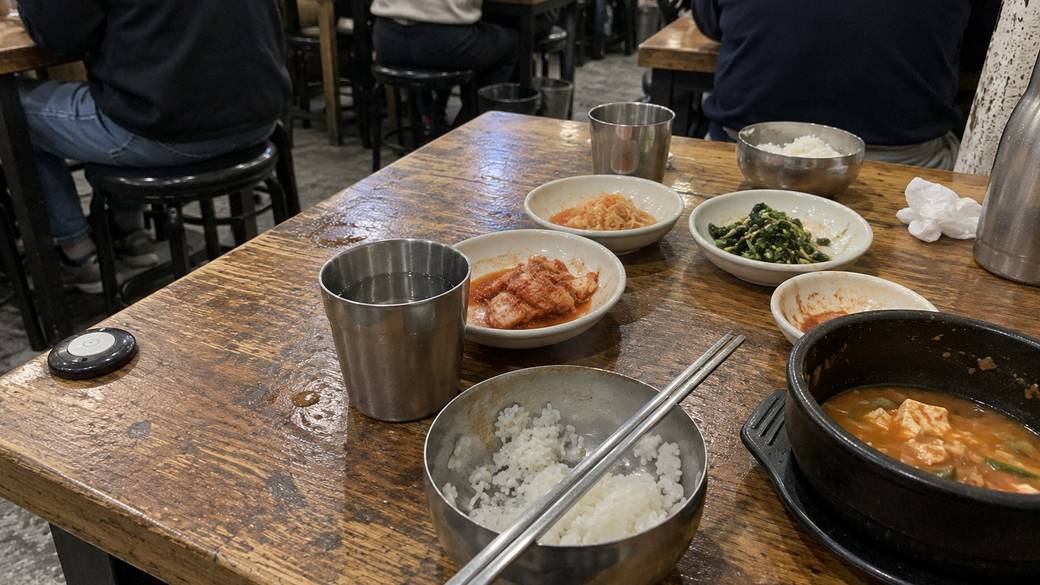 Steel water cups, rice bowls and small side dishes on a wooden table in a busy Seoul restaurant